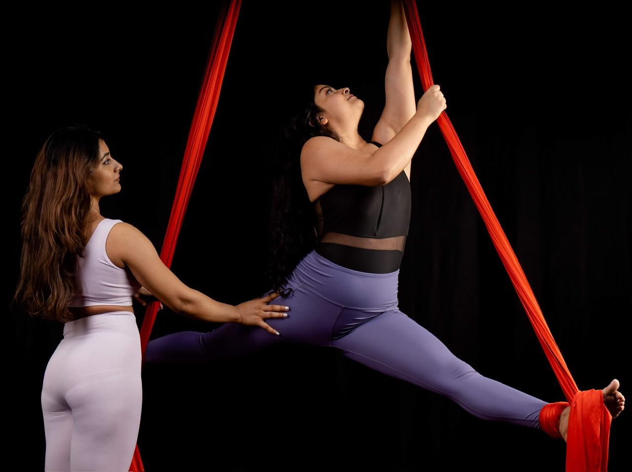 Roshani spotting a student holding a split on aerial silks